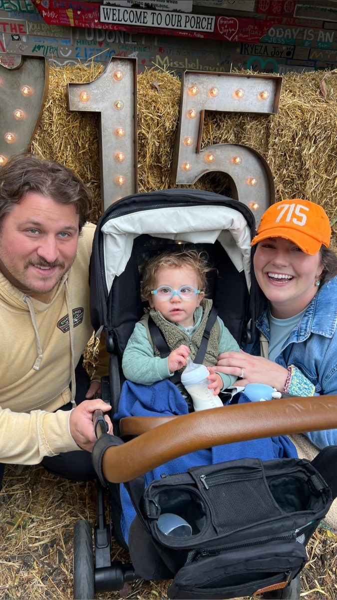 A family with their baby at the lit 715 marquee and hay bales