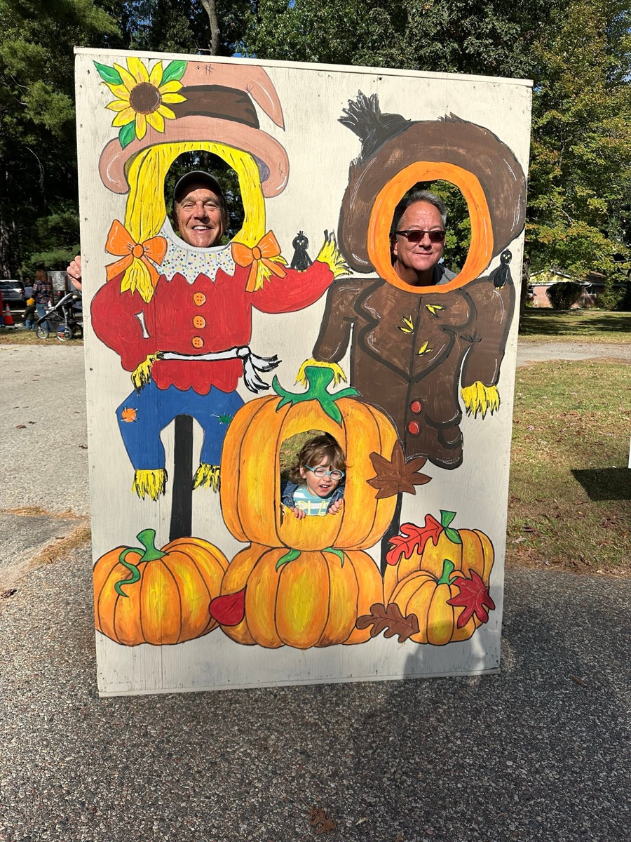 A child peeking through a scarecrow and pumpkin photo-op board